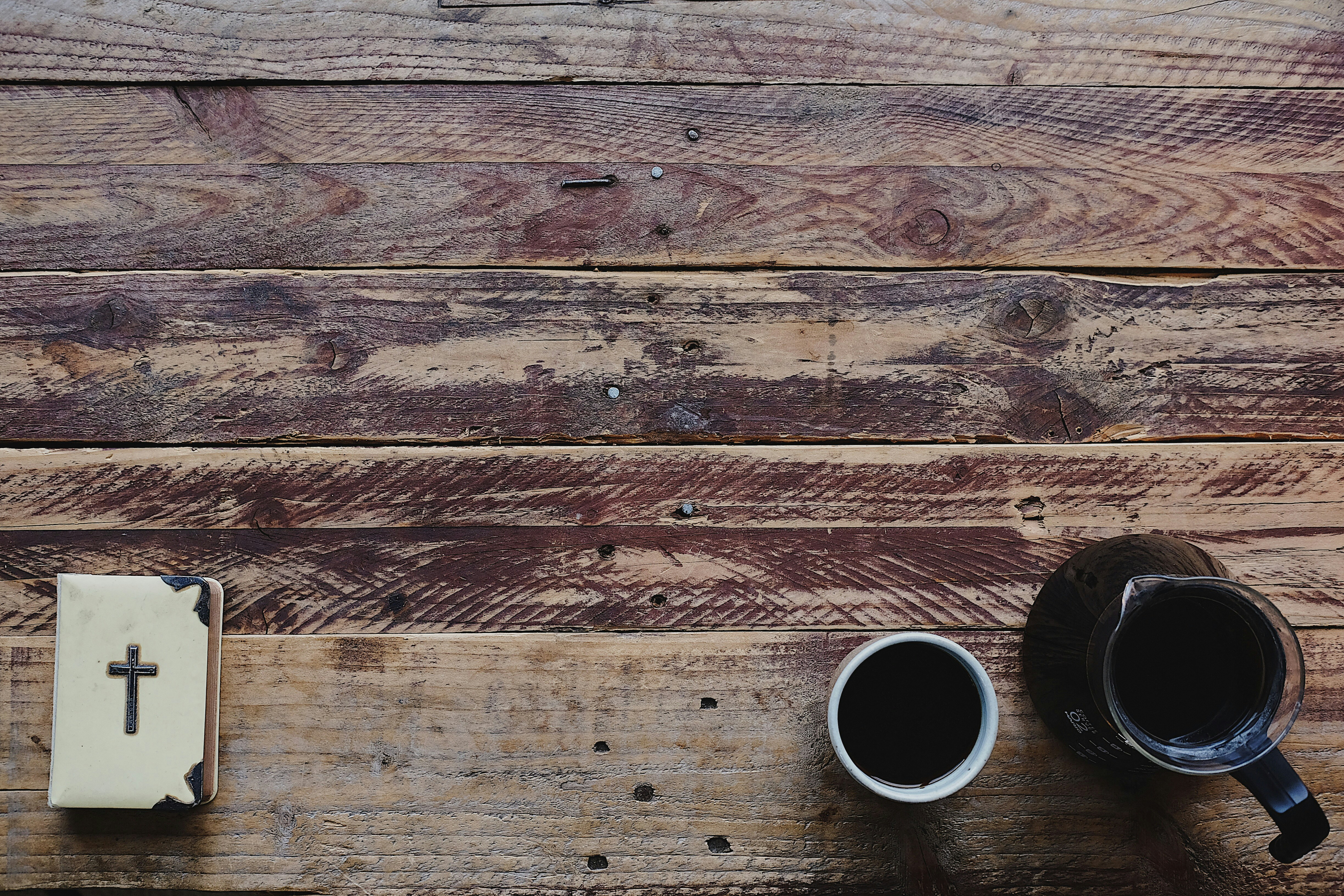 Bible, cross, and coffee cup on weathered wooden surface representing spiritual exploration.