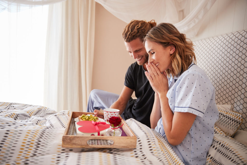 man surprising his female partner with breakfast and gifts in bed, close up