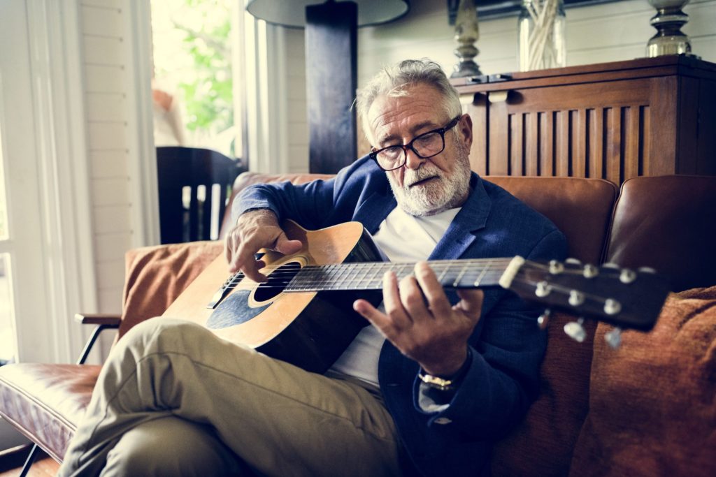 An elderly man is playing guitar