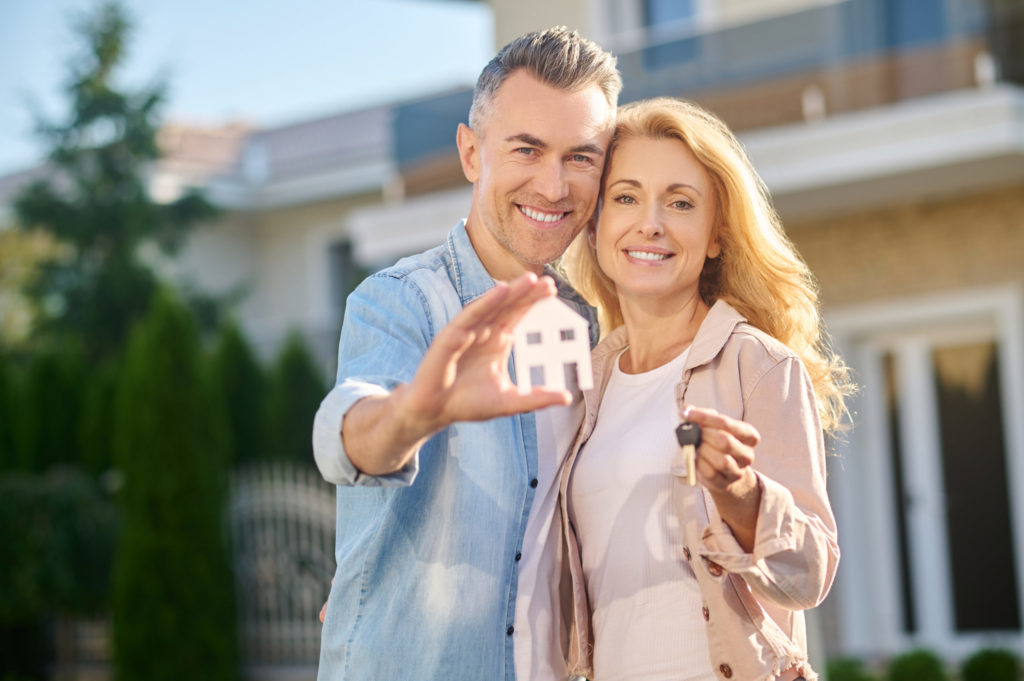 Man showing house sign and wife with key