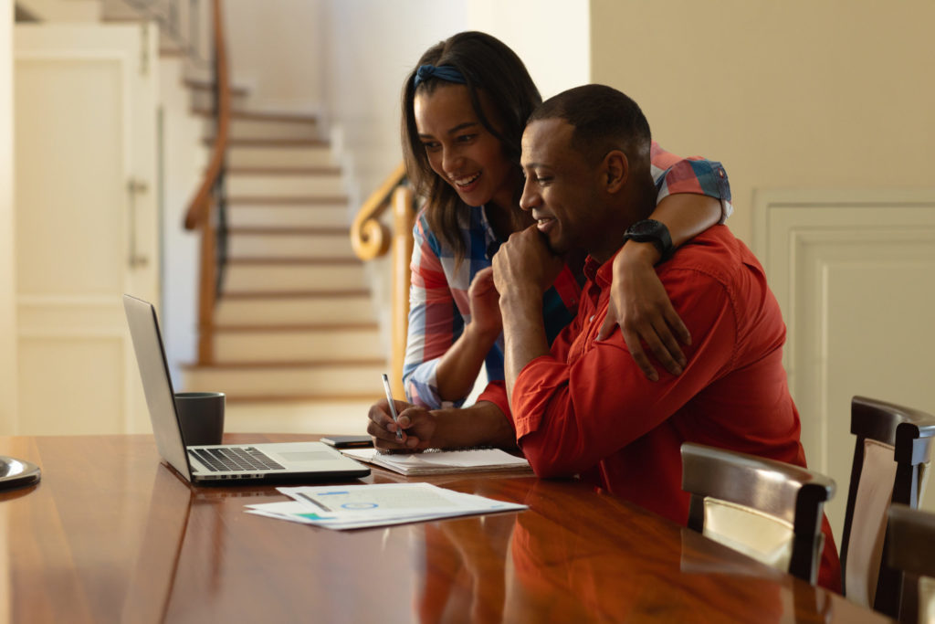 Smiling young african american couple planning home budget while sitting with laptop at table